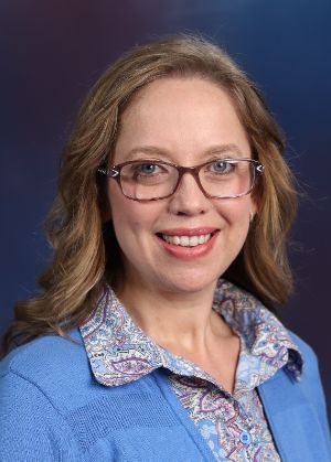Michelle Hummel, a caucasian woman with blond hair and glasses, smiling at the camera